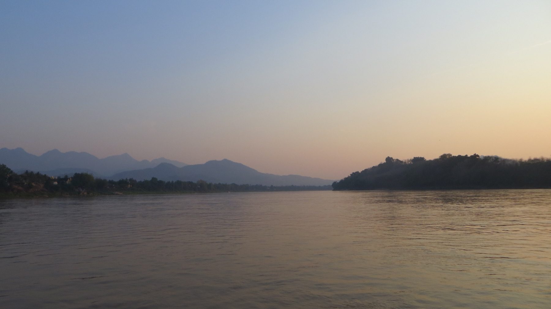 Reliefs boisés et ciel du soir reflétés dans les eaux calmes du fleuve.