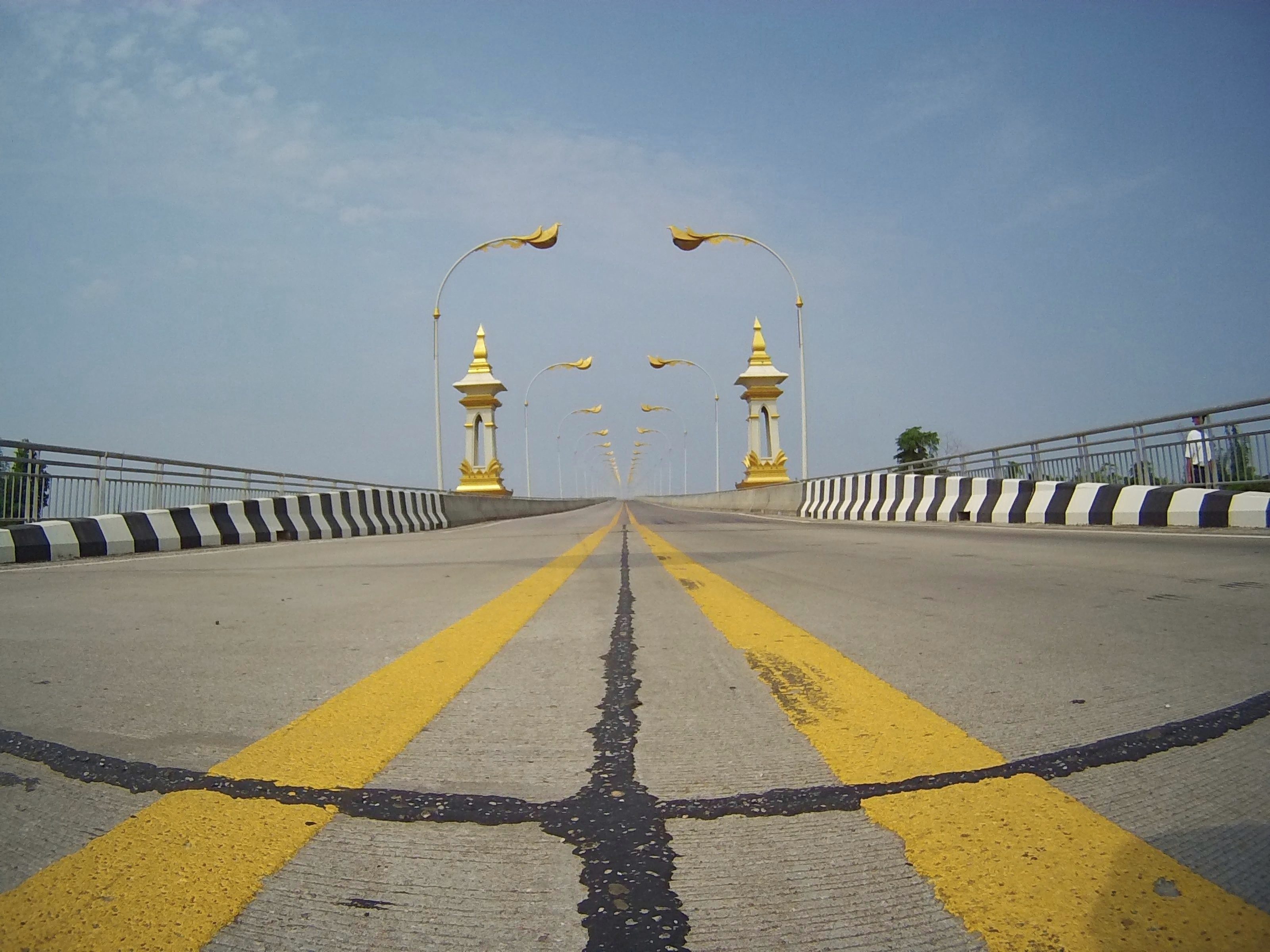 Route et pont ornés de détails dorés dessinant une perspective vers l’horizon au Laos.