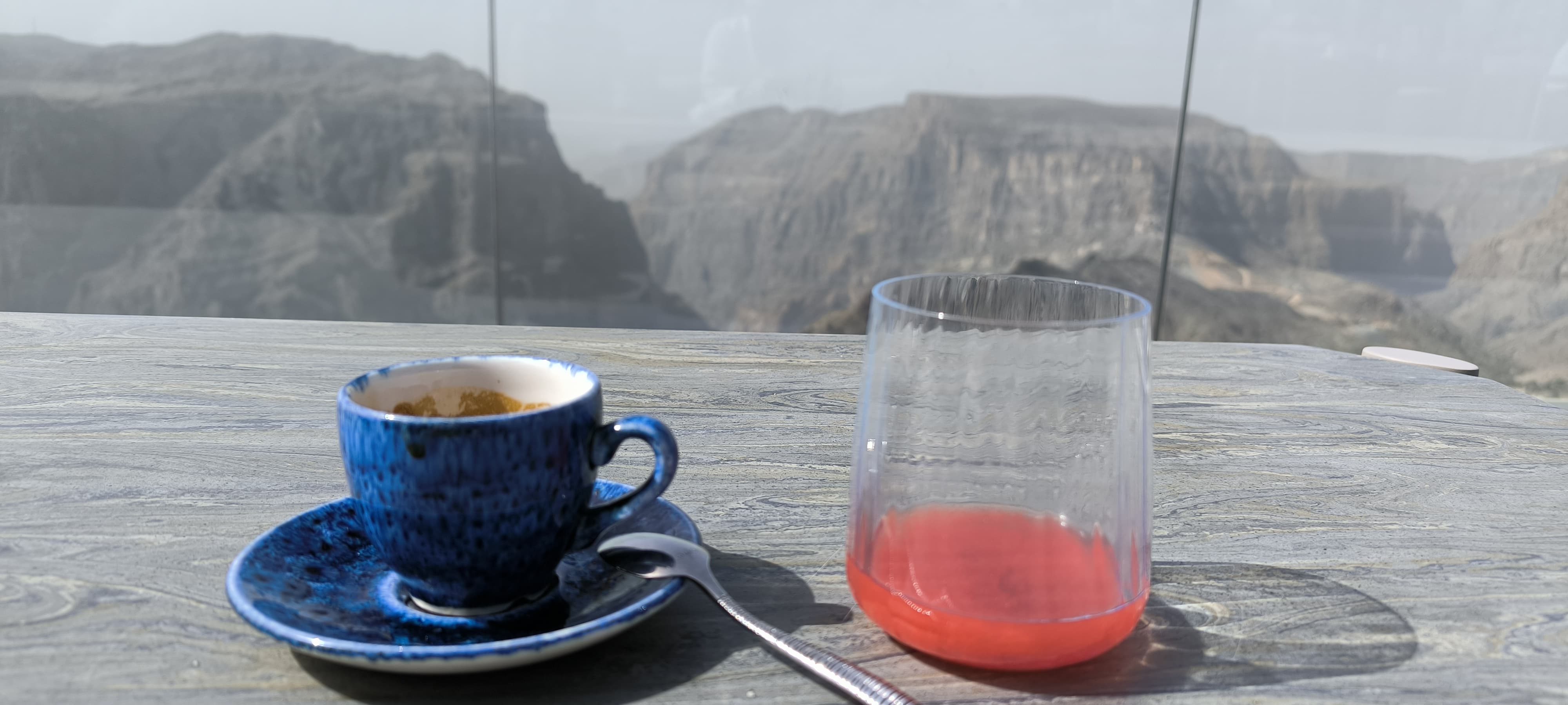 Tasse de café et verre posés sur une table face aux montagnes d’Oman