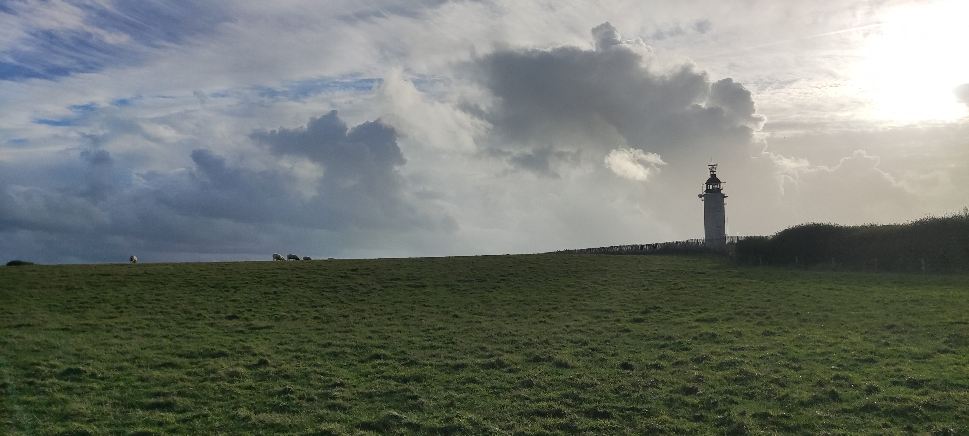 Phare isolé sous un vaste ciel nuageux au bord d’une prairie