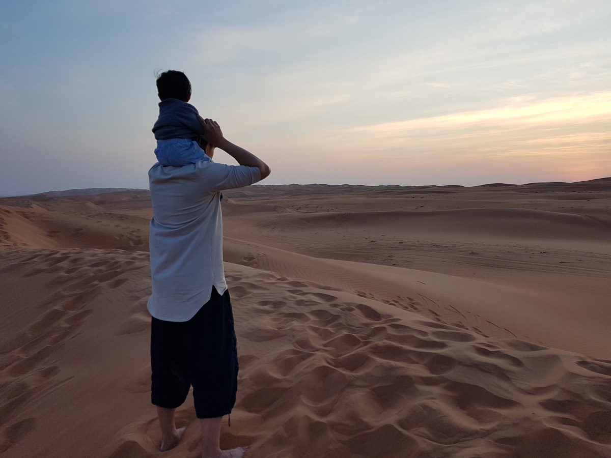 Père portant son enfant face aux dunes du désert omanais